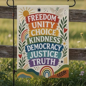 Puede incluir: Una bandera de jardín con las palabras "FREEDOM UNITY CHOICE KINDNESS DEMOCRACY JUSTICE TRUTH" en colores arcoíris. La bandera tiene un diseño de sol, paloma y arcoíris. Se muestra en un soporte de metal negro en un campo de hierba junto a una valla de madera.