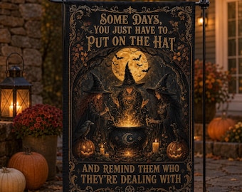 Può includere: Una bandiera da giardino rettangolare con tre streghe con cappelli a punta riunite attorno a un calderone luminoso sotto una luna piena. Il testo recita: SOME DAYS, YOU JUST HAVE TO PUT ON THE HAT AND REMIND THEM WHO THEY'RE DEALING WITH. Toni autunnali.