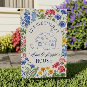 Puede incluir: Una bandera de jardín con un borde floral y el texto "LIFE IS BETTER AT Mimi & Poppi's HOUSE". El diseño presenta un dibujo lineal azul de una casa con un corazón y un círculo con el texto.