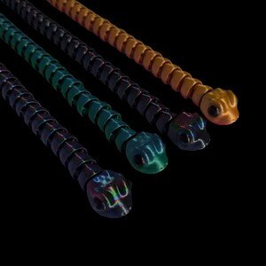 May include: Four flexible, segmented, plastic snakes in different colours: orange, black, green, and iridescent black. The snakes are arranged in a row, with the orange snake at the top and the iridescent black snake at the bottom.