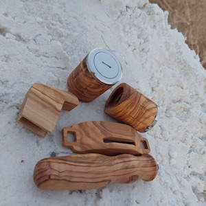 May include: A selection of handcrafted wooden items, including a cylindrical container with a silver lid, a small rectangular piece, and other uniquely shaped pieces. The wood has a natural grain pattern and a light brown colour.