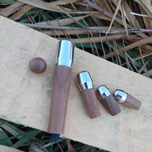 Puede incluir: Un conjunto de patas de muebles de madera con tapas de metal pulido. Las patas varían en tamaño y forma, con una pequeña bola de madera y una pata más grande con base roscada. La madera tiene un tono marrón cálido.