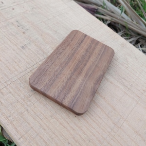 Może przedstawiać: Prostokątny drewniany podkładka z zaokrąglonymi rogami, prezentujący wzór ciemnobrązowego usłojenia drewna. Podkładka jest umieszczona na jasnej drewnianej powierzchni, z naturalnymi elementami w tle.