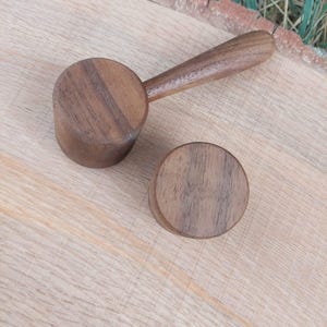 Könnte beinhalten: Ein hölzerner Kaffeelöffel mit Griff und eine separate, passende Holzscheibe. Der Löffel und die Scheibe sind aus dunkelbraunem Holz gefertigt und werden auf einer hellbraunen Holzoberfläche präsentiert.