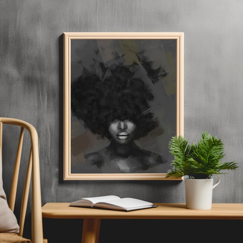 Puede incluir: Un retrato en blanco y negro enmarcado de una persona con un gran afro. La obra de arte est&aacute; en un marco de madera clara y cuelga de una pared gris. Una peque&ntilde;a planta en maceta y un libro abierto est&aacute;n sobre una mesa de madera frente a la obra.