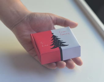 May include: A red and white gift box with a black and white Christmas tree design. The box says "To: Lisa" and "From: Tommy".