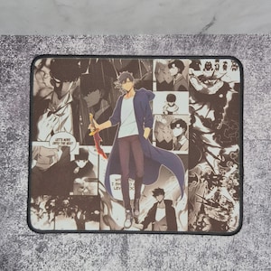 Könnte beinhalten: Rechteckiges Mauspad mit einer Illustration im Manga-Stil. Das Design zeigt eine Figur in einem langen blauen Mantel, die ein rotes Schwert hält, vor einer Collage von Comic-Panels. Das Mauspad hat einen schwarzen Rand und enthält Text.