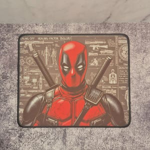 May include: Rectangular mouse mat featuring a detailed illustration of Deadpool in his signature red and black costume. The image includes two katanas and a background with technical diagrams and text. The mouse mat has a black border.