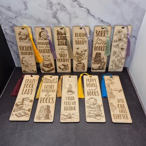 May include: Ten wooden bookmarks with colourful tassels. Each bookmark features a different book-themed design and quote. The quotes include "Fiction Addiction", "Bookmark are for quitters", "I have no shelf control", "Reading is my therapy", "Sorry I'm fully booked", "Crazy Book Lady", "Easily distracted by books", "I read past my bedtime", "Puppy, coffee and books", and "Just one more chapter".