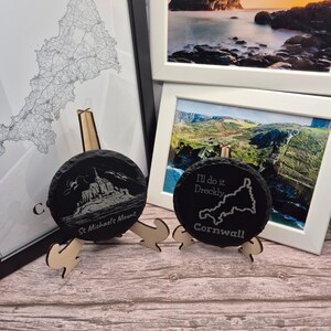 Peut inclure: Deux sous-verres en ardoise noire avec des motifs gravés. Le premier sous-verre présente une image du Mont Saint-Michel et le texte "St. Michael's Mount". Le deuxième sous-verre présente une carte de Cornouailles et le texte "I'll do it Drecldy Cornwall".