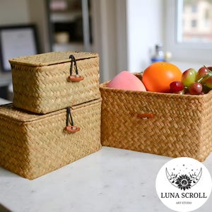 Puede incluir: Cestas de almacenamiento rectangulares tejidas en tonos naturales. Dos cajas con tapa y cierres de palanca de madera est&aacute;n apiladas junto a una cesta abierta m&aacute;s grande llena de fruta. Las cestas est&aacute;n hechas de un material tejido marr&oacute;n claro.