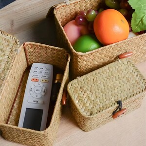 Puede incluir: Cestas de almacenamiento de hierba marina tejida en varios tama&ntilde;os. Una cesta contiene un mando a distancia y una botella peque&ntilde;a. Otra cesta contiene una naranja, uvas y una lima verde. Las cestas tienen cierres de palanca de madera.