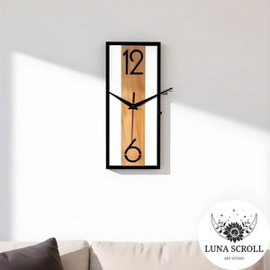 Peut inclure: Une horloge murale rectangulaire avec un cadre noir, un centre à grain de bois vertical et des bordures blanches. Le cadran affiche les chiffres noirs 12 et 6, avec des aiguilles noires. L'horloge est fixée sur un mur blanc.