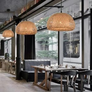 May include: A restaurant interior with a wooden table and chairs, a gray couch, and three woven pendant lights hanging from the ceiling.