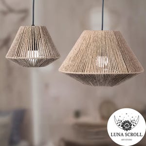 May include: Two pendant lights with beige rope shades. The shades have a geometric shape and are suspended from black cords. The lights are in a neutral-toned room, creating a warm and inviting atmosphere. The Luna Scroll Art Studio logo is in the bottom right corner.