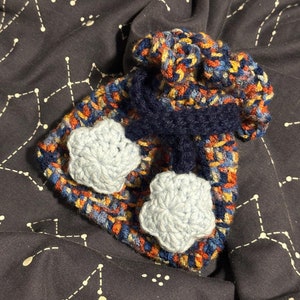 May include: A crocheted hat with a blue, red, and yellow pattern. The hat has two blue crocheted flower embellishments.