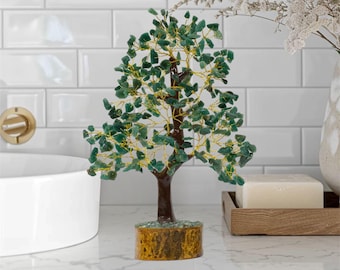 May include: A decorative tree sculpture with a brown trunk, green leaves, and a yellow base. The leaves are made of small, green stones. The tree is displayed on a white countertop.