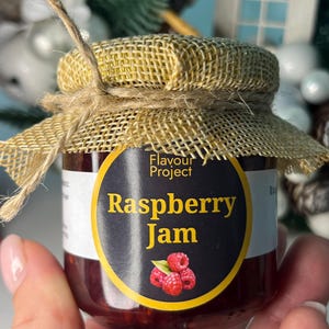 May include: A small jar of raspberry jam, with a burlap lid and twine tie. The label reads "Flavour Project Raspberry Jam" with a raspberry graphic. The jam is a deep red colour.