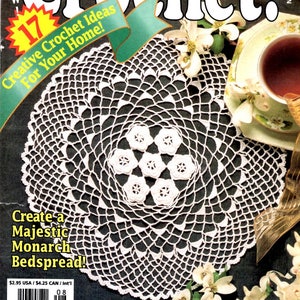 May include: The cover of a crochet magazine features a white, lacy doily with a floral center. Text includes "Hooked on Crochet!" and "Creative Crochet Ideas For Your Home!" along with the title "Thrill to a Symphony Doily!"