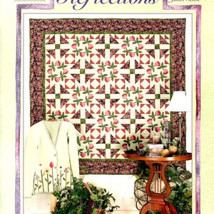 May include: A quilt pattern book titled "Reflections" by Janet Selck. The book cover features a quilt with a patchwork design of pink, green, and white triangles. The quilt is displayed on a table with a vase of flowers and a lamp.