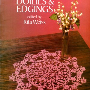 May include: A book titled "Tatting Doilies & Edgings" edited by Rita Weiss. The cover features a pink tatted doily on a wooden surface with a vase of white flowers.