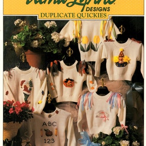 May include: A collection of white sweaters with various designs, including a Christmas tree, a pumpkin, a clown, and a bunny. The sweaters are displayed on hangers. The image also features the text "Alma Lynne Designs Duplicate Quickies."