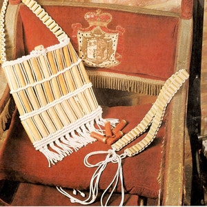 May include: A handcrafted bag and belt set made from light-coloured wooden beads and white string, with a fringed base. The bag is rectangular and the belt is long. The set is displayed on a red velvet chair.