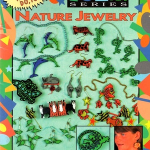 May include: A craft foam book cover titled "Nature Jewelry" with various jewelry examples. The jewelry includes earrings and necklaces with animal and nature-themed designs, such as dolphins, cats, and fish. The cover also includes the text "23 Projects Kids Can Do, Too!"