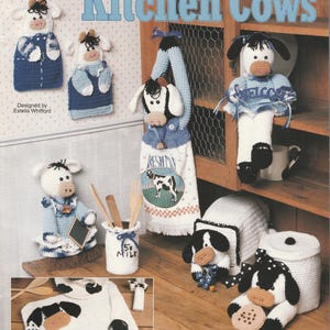 May include: A crochet pattern book titled "Kitchen Cows" featuring various cow-themed kitchen accessories. The image showcases crocheted cow-shaped pot holders, a towel, a milk bottle holder, and other decorative items in white, black, and blue.