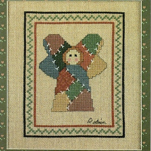 May include: A framed cross-stitch angel with patchwork wings and a smiling face. The angel is stitched with various colors, including blue, green, brown, and yellow. The artwork is framed with a green border featuring small heart-shaped designs.