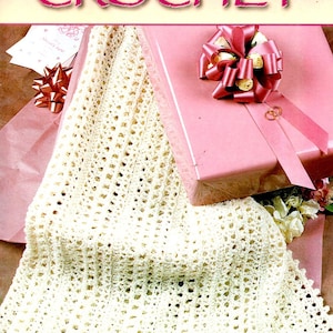 May include: A cream-colored crocheted blanket with a scalloped edge is draped over a pink gift box tied with a pink ribbon. The cover of "Annie's Favorite Crochet" magazine is visible in the background.