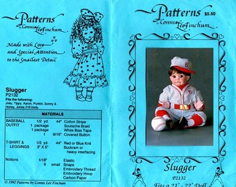 May include: A sewing pattern instruction sheet for a doll outfit titled Slugger P2132 by Connie Lee Finchum. The blue paper features a photograph of a doll wearing a white and blue pinstriped baseball uniform with a red cap and socks.