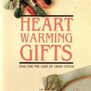 May include: A collection of embroidery floss in shades of green, red, and pink, alongside a wooden embroidery hoop, metal scissors, and fabric. The text reads HEART WARMING GIFTS From FOR THE LOVE OF CROSS STITCH and SUPPLEMENT TO FOR THE LOVE OF CROSS STITCH.