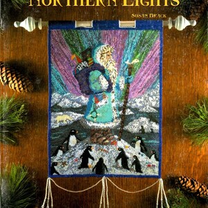 May include: A beaded wall hanging titled Enchanted Santas Vol. 2 Issue 2 Northern Lights by Susan Brack. It features a Santa figure in a blue coat with a staff and pack, surrounded by penguins and a polar bear against a purple aurora background.