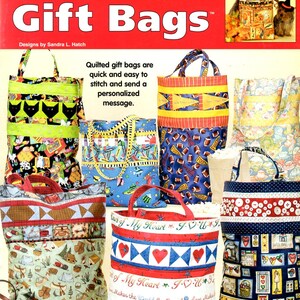 May include: A book cover featuring various quilted gift bags with different patterns and colors. The title reads "Four-Hour Quilted Gift Bags." The bags showcase diverse designs, including cats, footballs, and hearts. The text on the bags includes phrases like "Sealed with a Kiss."