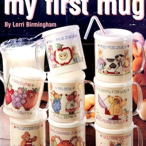 May include: A stack of clear plastic mugs with cross-stitch designs. Each mug features a different design, including an apple, cow, and bear. The mugs have lids and handles. Text on the mugs includes "My Apple Juice" and "Hurry for You". The cover reads "my first mug".