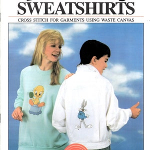 May include: A vintage Looney Tunes sweatshirt and jacket pattern. The sweatshirt is light blue with a Tweety Bird design. The white jacket features a Bugs Bunny graphic. The image includes the text "SWEATSHIRTS" and "CROSS STITCH FOR GARMENTS USING WASTE CANVAS".