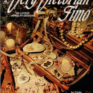 May include: A book cover with the title "Very Victorian Fimo" and the text "30 Lovely Jewelry Designs" in a gold and white font. The cover features a wooden box with a variety of jewelry pieces made from polymer clay, including flowers, hearts, and butterflies. The jewelry is displayed on a white lace doily and a wooden surface.