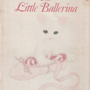 May include: A cross-stitch pattern titled "The Little Ballerina" featuring a white cat with blue eyes and pink ballet shoes. The design is on a light pink fabric with the Leisure Arts logo.