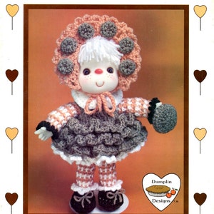 May include: A handmade doll named "Oatmeal Cookie" with a crocheted bonnet adorned with gray circles. The doll has a white face, rosy cheeks, and a ruffled gray skirt. The text "Oatmeal Cookie" and "Brought to you directly from Lollipop Lane" are visible.