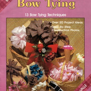 May include: A book cover titled "Secrets of Bow Tying" with various bows displayed in baskets. The cover is pink with text and images of bows. The book features 13 bow tying techniques and over 20 project ideas.