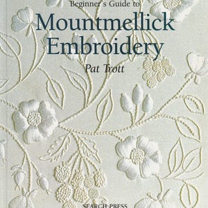 May include: A book titled Beginner's Guide to Mountmellick Embroidery by Pat Trott. The cover is off-white with raised, monochromatic white floral and berry embroidery patterns featuring leaves, stems, and blossoms across the surface.