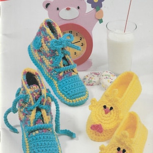 May include: Image of a book cover titled "Creature Comforts" featuring crochet slipper patterns. The image shows blue and yellow crochet sneakers and yellow chick-shaped slippers. A pink bear-shaped clock and a glass of milk are also visible.