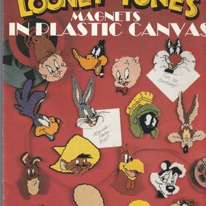 May include: A craft leaflet titled Looney Tunes Magnets in Plastic Canvas featuring various cartoon character designs. The cover displays stitched plastic canvas magnets of characters like Bugs Bunny, Tweety, and Daffy Duck on a red background.