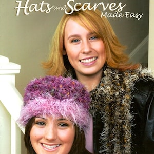 May include: Two women, one wearing a pink and purple fuzzy hat and the other wearing a brown and white fuzzy scarf, are shown on the cover of a book titled "Novelty Yarn Locker Hooking Hats and Scarves Made Easy".