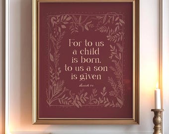 May include: A framed print with the text "For to us a child is born, to us a son is given" in a decorative floral border. The print is in a gold frame and hangs above a fireplace decorated with greenery and candles.
