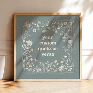 May include: Square framed art print with a light teal background and a floral border. The text "your custom quote or verse" is centered in white. The frame is a light wood color.