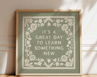 May include: A framed print with the text "IT'S A GREAT DAY TO LEARN SOMETHING NEW" in white. The text is centered on a sage green background, surrounded by a white floral border. The frame is a light wood color.