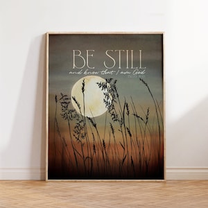 May include: A beige and brown watercolor print with a full moon and tall grass silhouetted against a sunset sky. The print features the text "Be Still and know that I am God" with the scripture reference "Psalm 46:10".