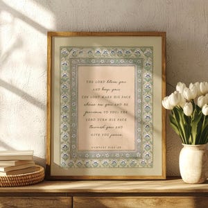 Peut inclure: Une impression murale encadrée présentant le texte de Nombres 6:24-26 dans une police serif. L'impression a un fond pêche clair et une bordure décorative avec des motifs floraux bleus et verts. Le cadre est en bois brun clair.